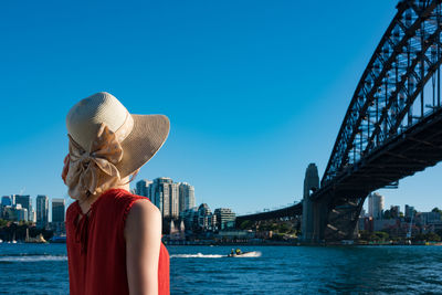 Side view of woman looking bridge in city against clear blue sky