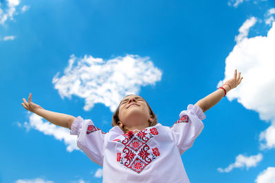 Low angle view of girl with arms raised against sky