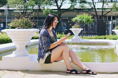 Side view of young woman sitting on retaining wall