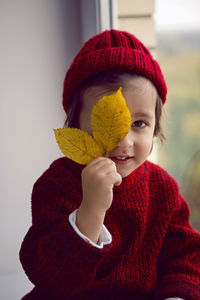 Boy child in red knitted sweater and hat sitting on the window in autumn