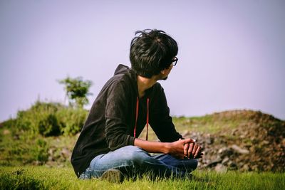 Side view of man sitting on field against clear sky