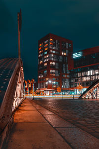 Illuminated footpath amidst buildings in city at night