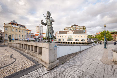 Statue on footpath in city against sky