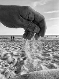 Cropped hand pouring sand at beach against sky
