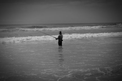 Man fishing in sea against sky