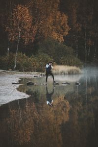 Reflection of man photographing on lake in forest