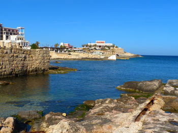 Scenic view of sea by buildings against clear blue sky