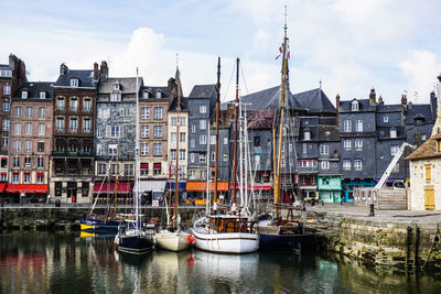 Sailboats moored on river by buildings against sky