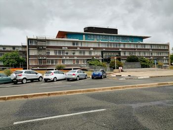 Cars on road by buildings in city against sky