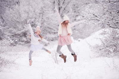 Full length of sibling jumping over snow cover land