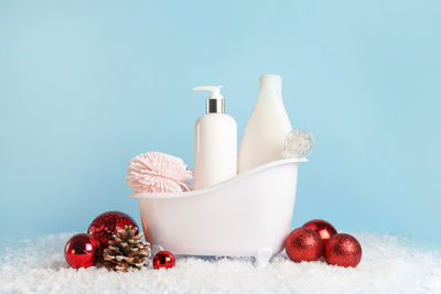 White bathtub with cosmetics, body care products and christmas baubles on pastel blue