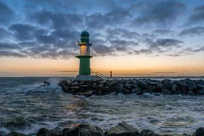 Lighthouse amidst sea against sky during sunset