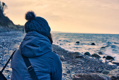 Rear view of man looking at sea shore during sunset