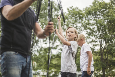 Siblings assisting father in making tent at camping site