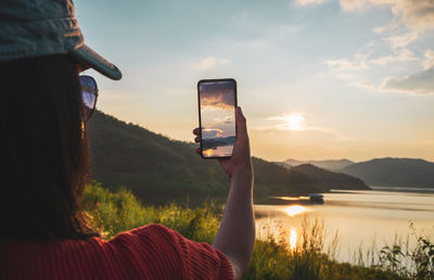 Woman photographing on smart phone against sky