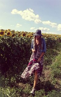 Full length of woman walking on sunflower field against sky