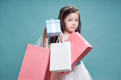 Portrait of a smiling girl holding gifts against blue background