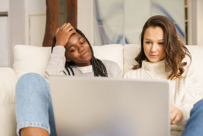 Smiling young women smiling while using laptop sitting on sofa at home