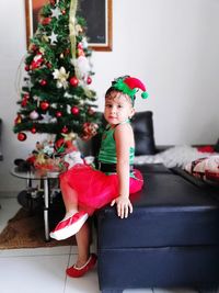 Portrait of cute girl sitting on sofa by christmas tree at home