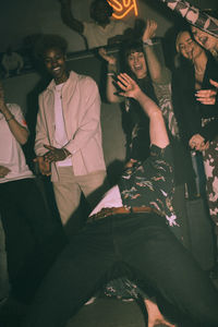 Young men and women cheering friend dancing while bending backwards at nightclub