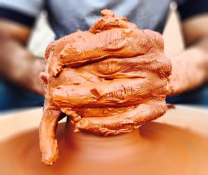 Midsection of man making earthenware on pottery wheel at workshop