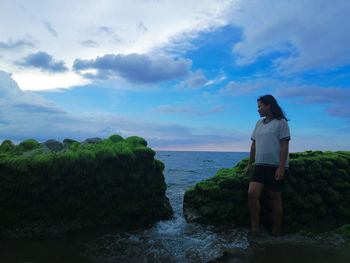 Woman standing by rock in sea against sky