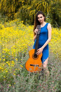 Beautiful woman holding guitar while standing amidst flowers