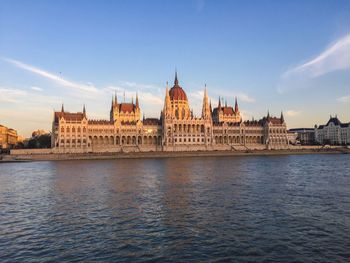Hungarian parliament building by danube river against sky during sunset