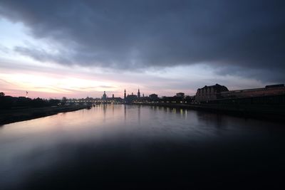 Scenic view of river by buildings against sky at sunset