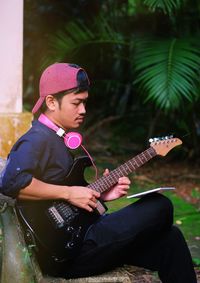 Young man playing guitar while sitting in park