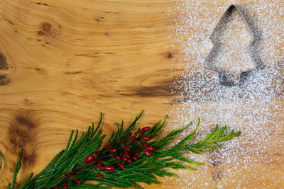 Directly above shot of pine needles with cookie cutter and flour on wooden table during christmas