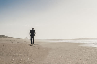 Silhouette of a solitary man taken from behind walking in an empty beach