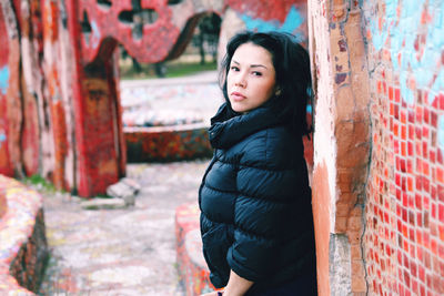 Portrait of beautiful young woman standing by wall