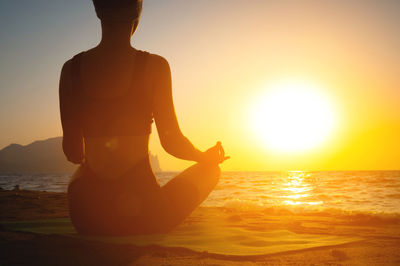 Rear view of silhouette woman standing at beach against sky during sunset