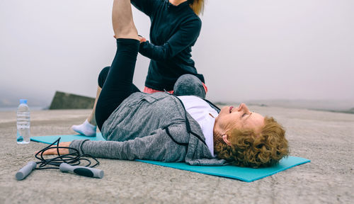 Daughter assisting mother in exercising at beach against sky