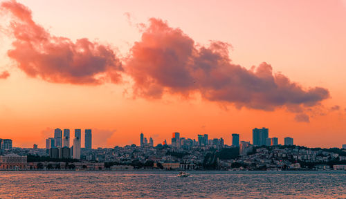 Scenic view of sea by buildings against sky during sunset