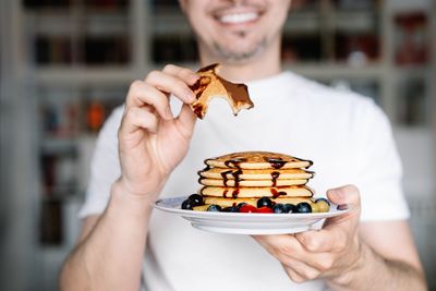 Midsection of smiling man holding pancakes in plate