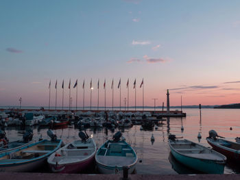 Boats moored in harbor at sunset