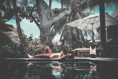 Woman relaxing on swimming pool against trees