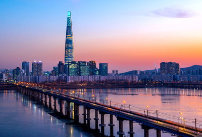 Illuminated modern buildings in city against sky during sunset