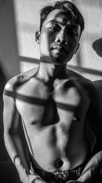 Portrait of shirtless man standing against wall