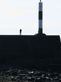 Silhouette man standing by lighthouse against sky
