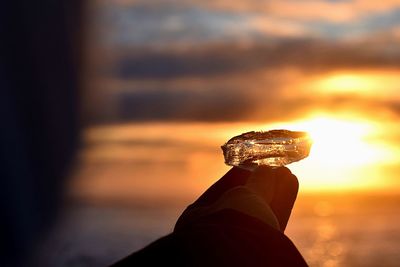 Close-up of hand holding orange against sky during sunset