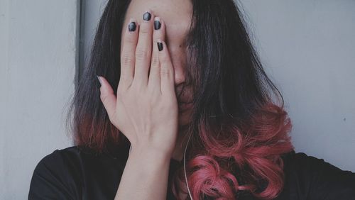 Woman covering face with eyes against wall