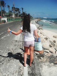 Rear view of young woman hailing taxi on road by beach