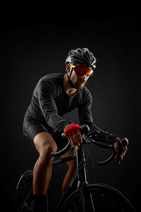 Athlete riding bicycle against black background