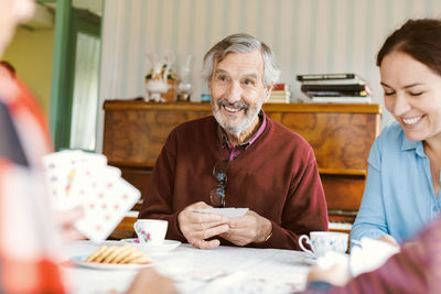 Smiling senior man playing cards with family at home