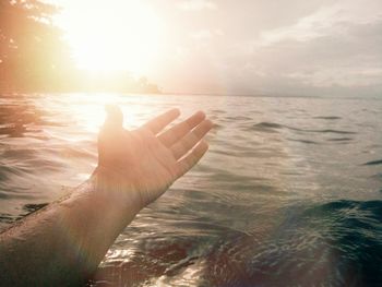 Close-up of hand against sea during sunset