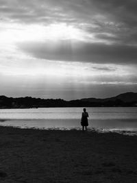 Rear view of a girl standing on the shore of a pond during an idyllic cloudy sky with filtering rays