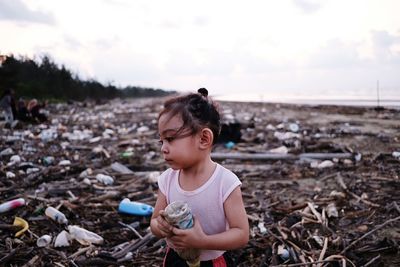 Girl holding bottle at dirty beach